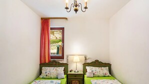 Una habitación con dos camas individuales, una mesita de noche con lámpara, un candelabro y una ventana con vistas a un jardín.