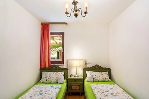 Ein Zimmer mit zwei Einzelbetten, einem Nachttisch mit Lampe, einer Deckenleuchte und einem Fenster mit Gartenblick.