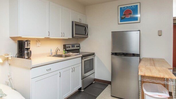 A compact kitchen with white cabinets, a microwave, a stainless steel refrigerator, and a coffee maker.