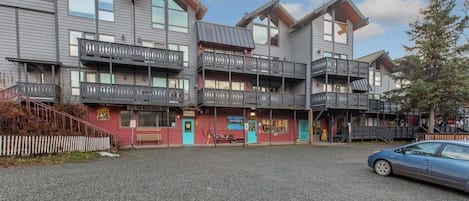 A multi-story building with balconies, a bakery shop, and a parking area.