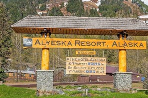 A wooden sign with 'Alyeska Resort, Alaska' and directional arrows pointing to 'The Hotel Alyeska & Tramway 1 MI' and 'Ski Resort, Daylodge & Parking 1 MI'. - Slopeside Studio Above The Bake Shop (Girdwood)