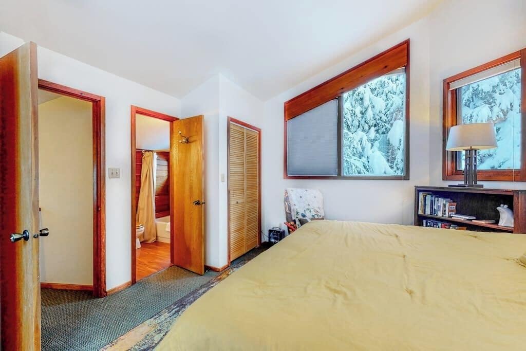 A bedroom with a bed, a wardrobe, a mirror, and a window with a view of trees.