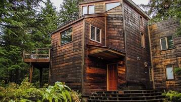A rustic wooden cabin with a balcony, a front door, and a staircase leading up to the entrance.