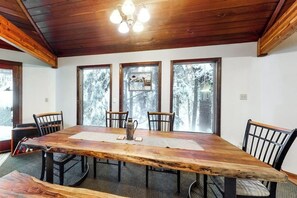 A wooden dining table with chairs, large windows, and a chandelier. - Open-beam Girdwood Chalet w/ Sunlit Solarium (Girdwood)