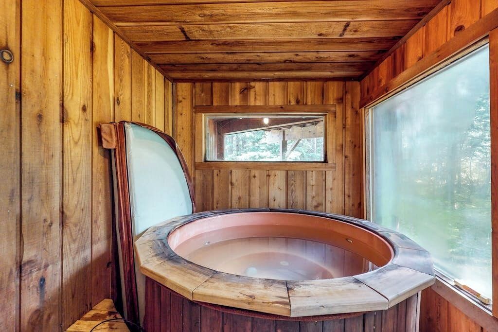 A wooden cabin interior with a hot tub, a window, and a wooden ceiling.