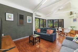 A spacious living area with a dark grey wall, a blue sofa, a wooden coffee table, and a grey armchair. - Palms Bungalow Nightcliff with Pool | 2BD, 2BTH (Nightcliff)
