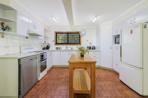A modern kitchen with white cabinetry, a wooden table, and a window with a view of greenery.