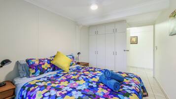 A bedroom with a bed, a nightstand, a lamp, a wardrobe, and a door leading to another room.