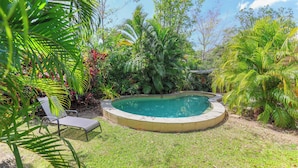 Una piscina envoltada de vegetació exuberant, amb una cadira de gandules i una petita zona de solàrium.