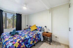 Ein Schlafzimmer mit Bett, Nachttisch, Lampe und einem Fenster mit Vorhängen.