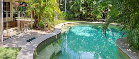 Une piscine entourée d’une végétation luxuriante, avec un espace abrité sur le côté gauche.
