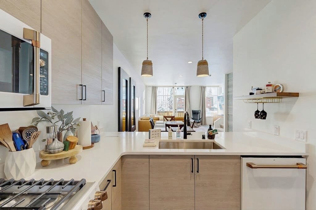 Een moderne keuken met een centraal eiland, hanglampen en uitzicht op de woonkamer.