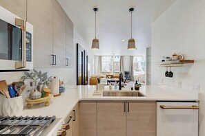 A modern kitchen with a central island, pendant lighting, and a view into the living area. - Newly Built Creek-side Townhome Near Girdwood Merc (Girdwood)