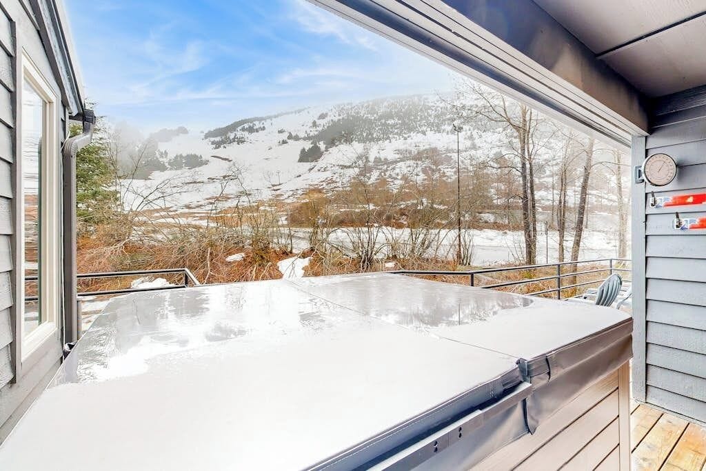 Een hottub op een houten terras met uitzicht op een besneeuwd landschap.