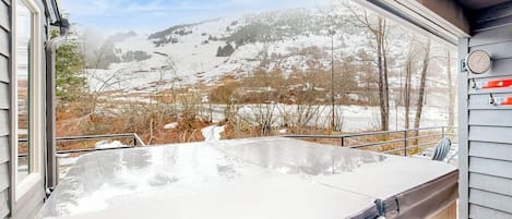 A hot tub on a wooden deck with a view of a snowy landscape.