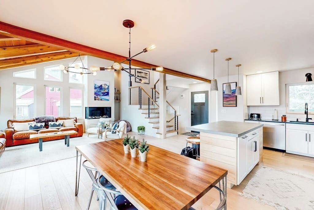 Een ruime woonkamer met een houten eettafel, een bank en een trap naar een verdieping boven.