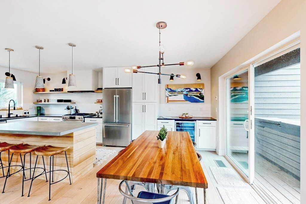 A modern kitchen with a wooden island, stainless steel appliances, pendant lighting, and a large window.