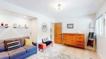 A living room with a sofa, a coffee table, a wooden dresser, and a door leading to another room.