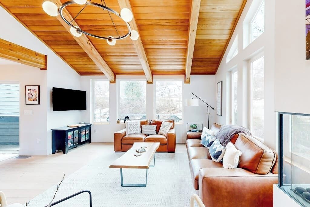 Een moderne woonkamer met een houten plafond, leren banken, een salontafel en grote ramen.