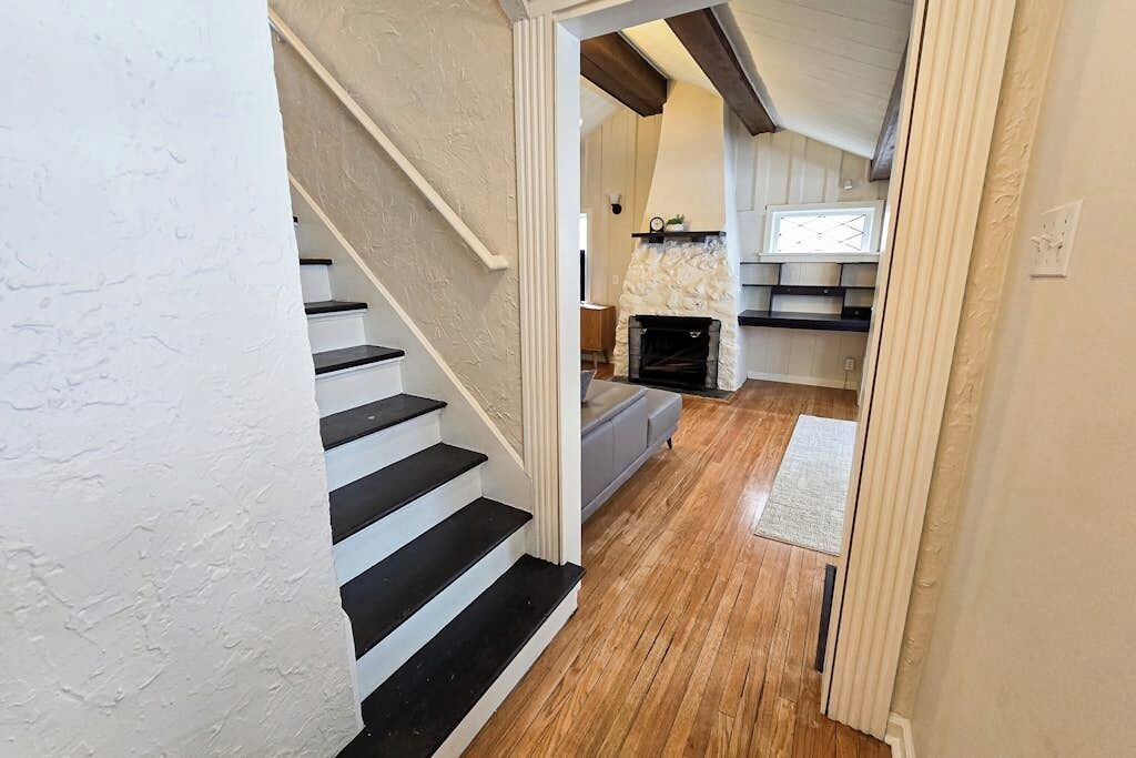 A staircase leading to a living area with a fireplace, wooden flooring, and a view of the outdoors.