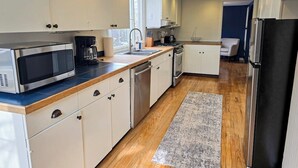 Una cocina moderna con gabinetes blancos, un microondas de acero inoxidable, una cafetera y un refrigerador.