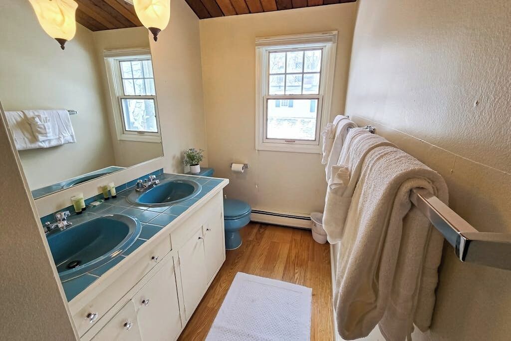 A bathroom with two sinks, a toilet, a towel rack, and a window.