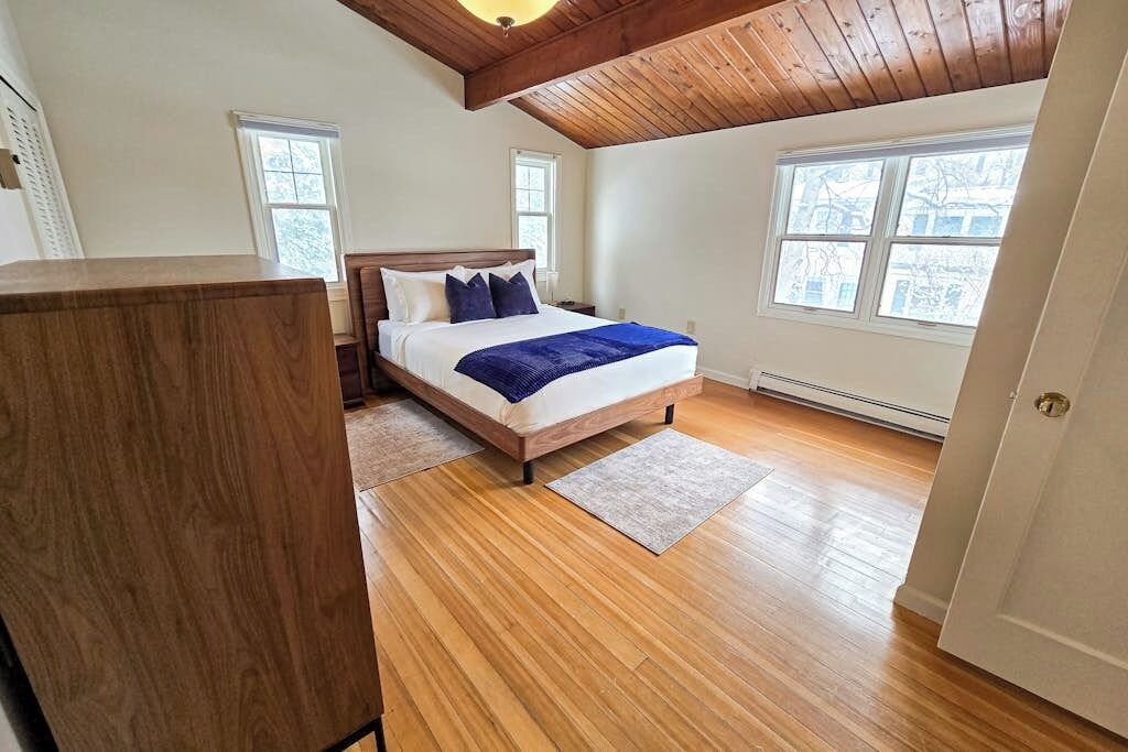A bedroom with a wooden floor, a bed with a blue blanket, and a wooden ceiling.