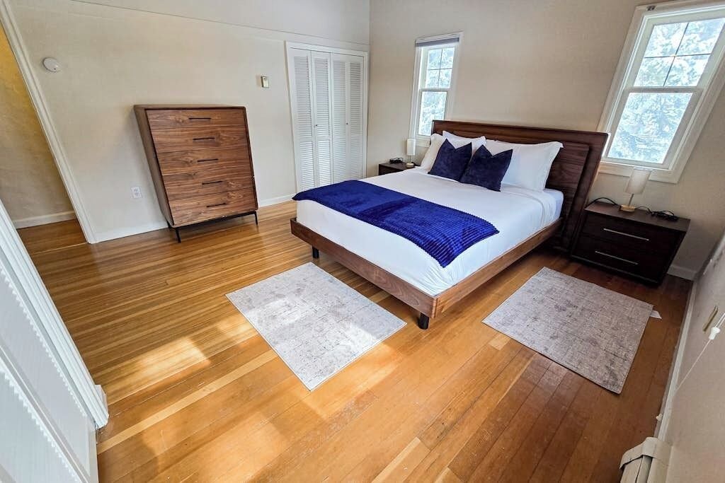A bedroom with a wooden bed, two nightstands, a dresser, and a window.