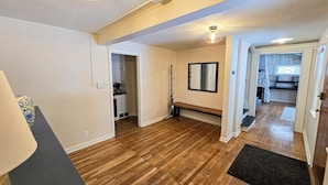 Una habitación con suelo de madera, un banco, un espejo y una puerta que da a otra estancia.