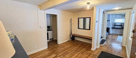 A room with wooden flooring, a bench, a mirror, and a door leading to another room.