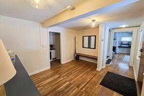 Ein Zimmer mit Holzboden, einer Bank, einem Spiegel und einer Tür zu einem anderen Raum.