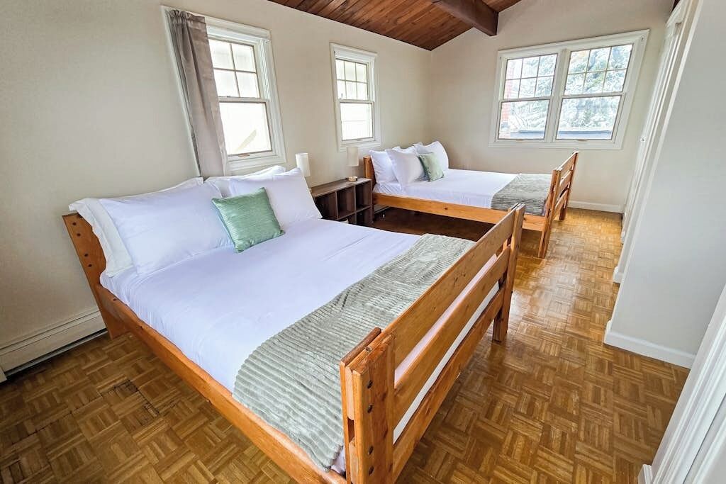 A room with two wooden beds, a wooden floor, and windows with curtains.