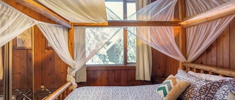 Een kamer met een bed, houten wanden, een raam en een hemelbed.