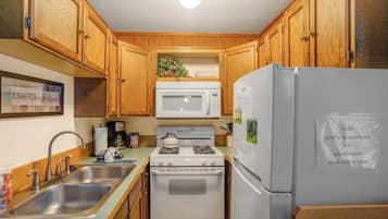 Una cocina compacta con armarios de madera, microondas, estufa y refrigerador.
