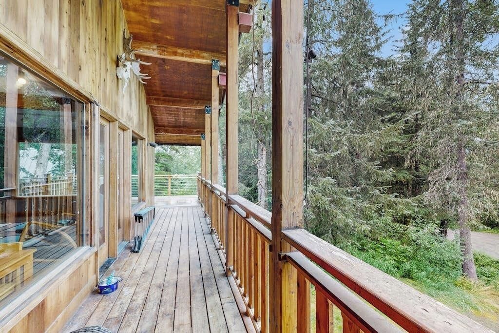 A wooden deck with glass railings overlooking a forested area.