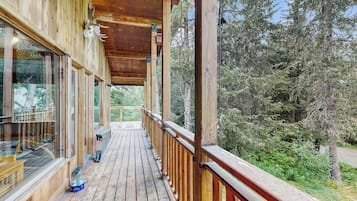 A wooden deck with glass railings overlooking a forested area.