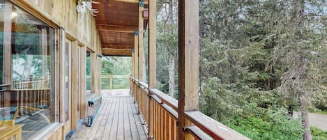 A wooden deck with glass railings overlooking a forested area.