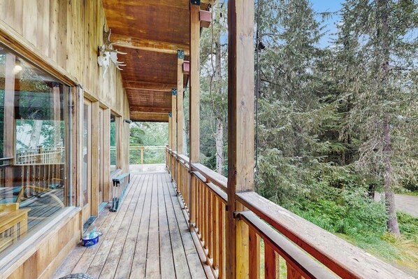 Una terraza de madera con barandillas de vidrio que da a un área boscosa.
