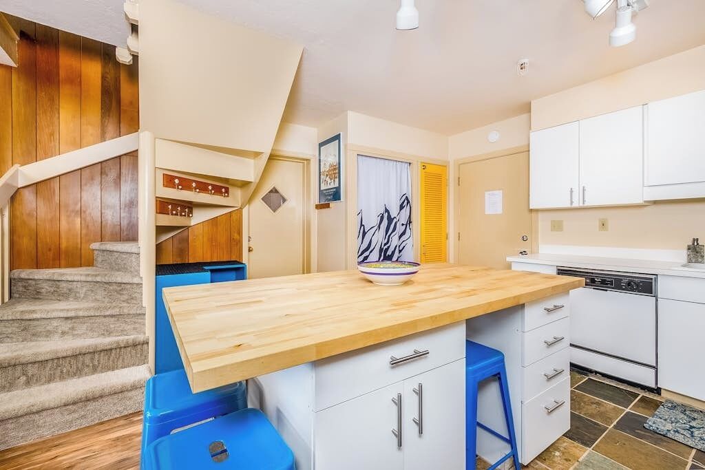 Una cocina con una isla de madera, armarios blancos y un taburete azul.