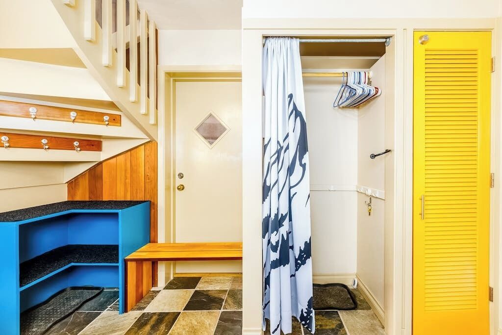 Ein Zimmer mit einer Treppe, einer Bank, einer Tür mit gelbem Griff und einem Vorhang mit Muster.