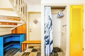 Una habitación con una escalera, un banco, una puerta con pomo amarillo y una cortina estampada.
