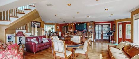 A spacious living area with a wooden staircase, a dining table with chairs, and a red sofa.