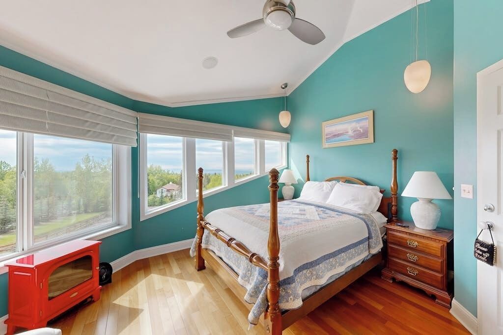 A bedroom with a four-poster bed, a nightstand, a lamp, a window with blinds, and a view of the outdoors.