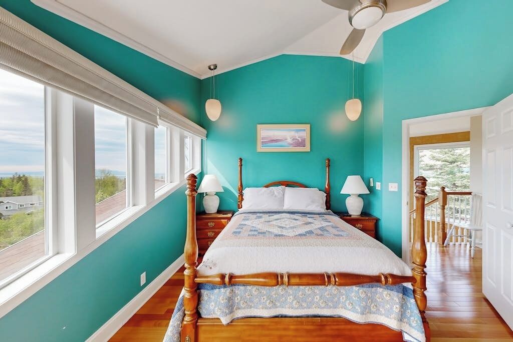 A bedroom with a large bed, two bedside tables, a ceiling fan, and a view of the outdoors.