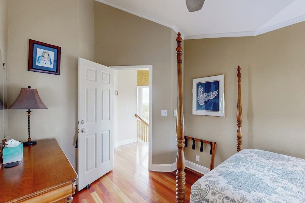 A bedroom with a four-poster bed, a wooden dresser, and a door leading to another room.