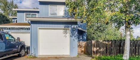 A two-story residential building with a garage, a driveway, and a wooden fence.