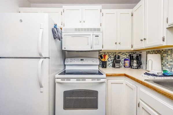 A compact kitchen with a refrigerator, microwave, stove, and a coffee maker on the countertop.