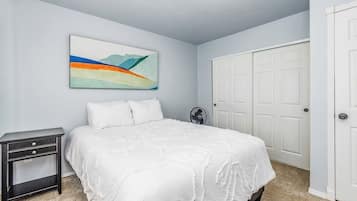 A bedroom with a bed, a nightstand, a wall-mounted fan, and a door.