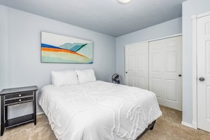 A bedroom with a bed, a nightstand, a wall-mounted fan, and a door.