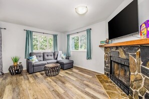 A living room with a stone fireplace, grey sofa, and a flat-screen TV.